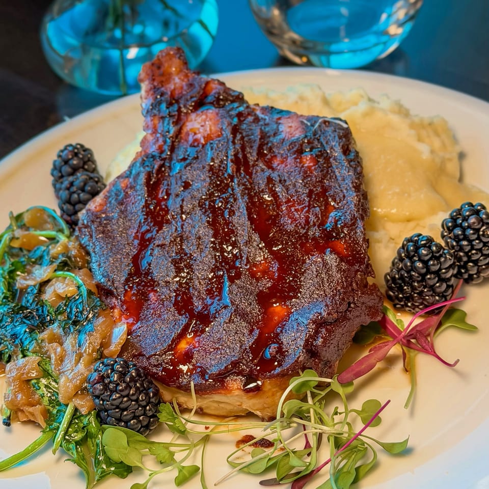 BBQ ribs with mashed potatoes, sauteed greens, and fresh blackberries on a white plate.