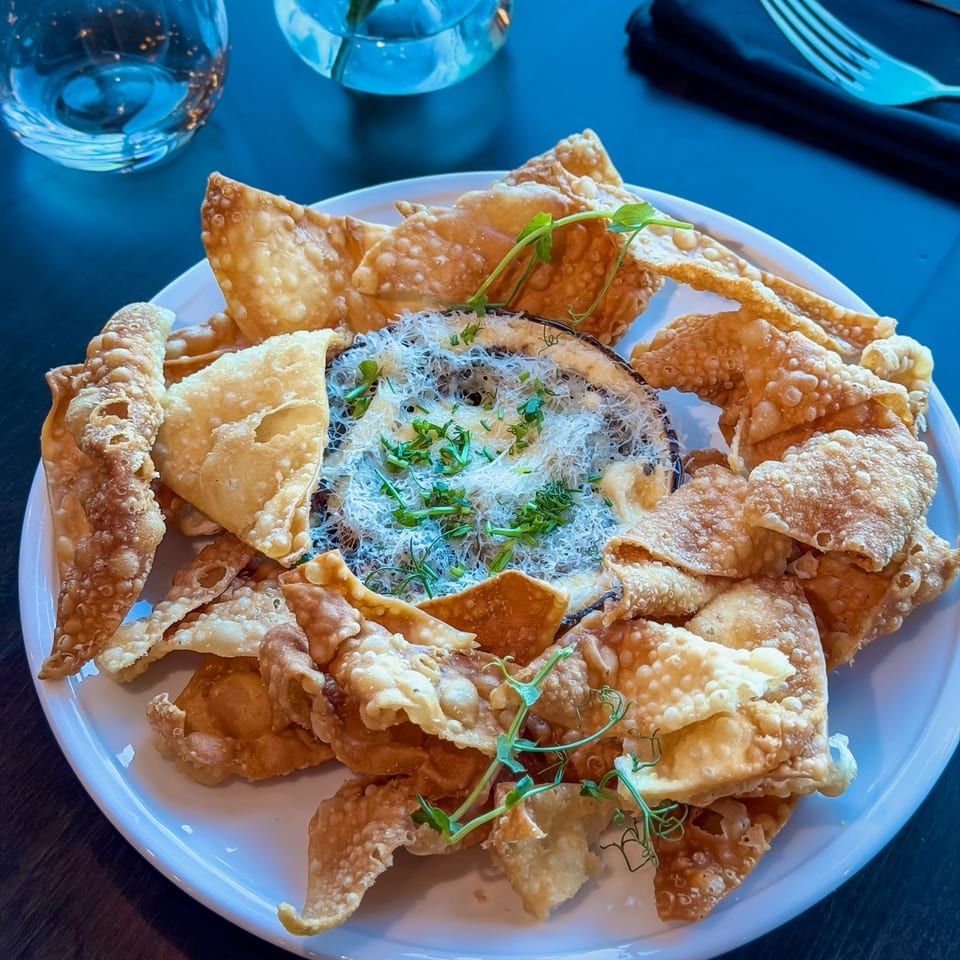 Crispy wonton chips surround a dip topped with shredded cheese and fresh herbs on a white plate.