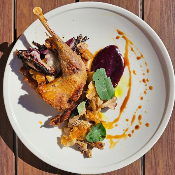 Crispy roasted quail with purple puree, mushrooms, and greens on a white plate at Rivage Oak Kitchen.