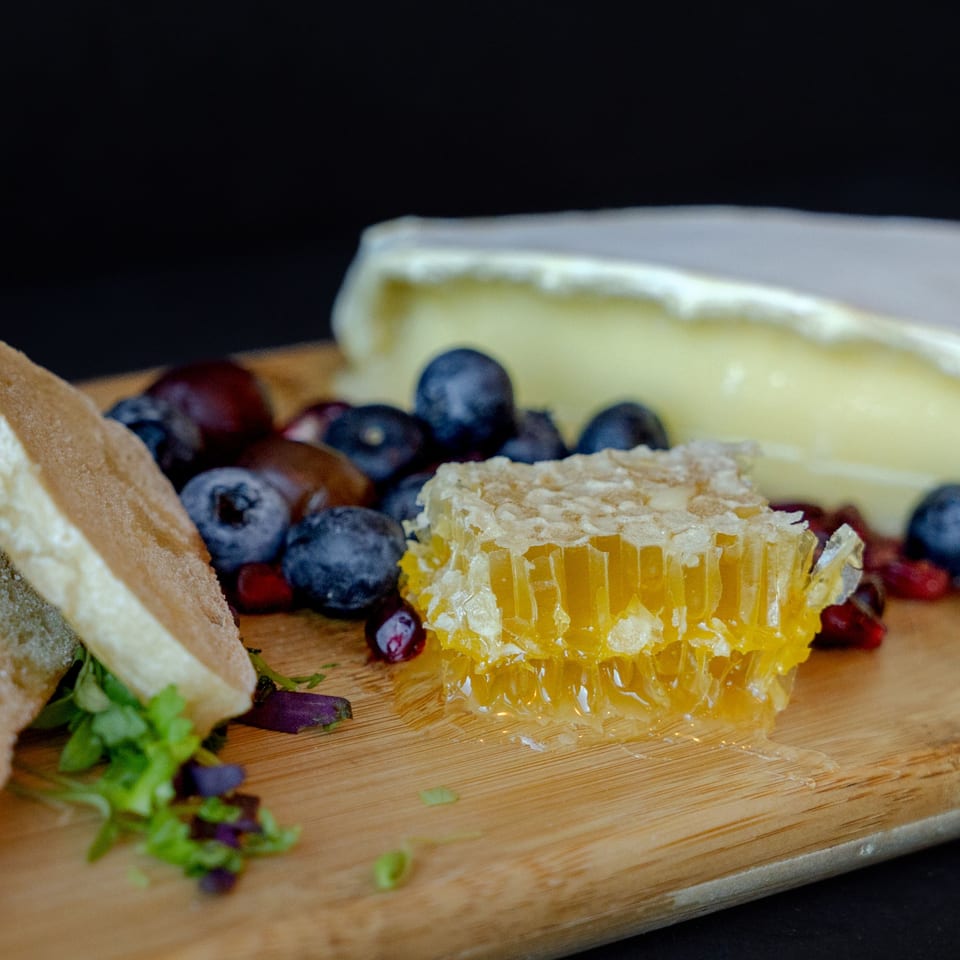 A charcuterie board with brie cheese, fresh blueberries, pomegranate seeds, honeycomb, and bread.