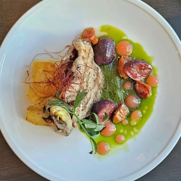 Fine-dining dish with grilled fish, roasted vegetables, green sauce, and orange spheres on a white plate.