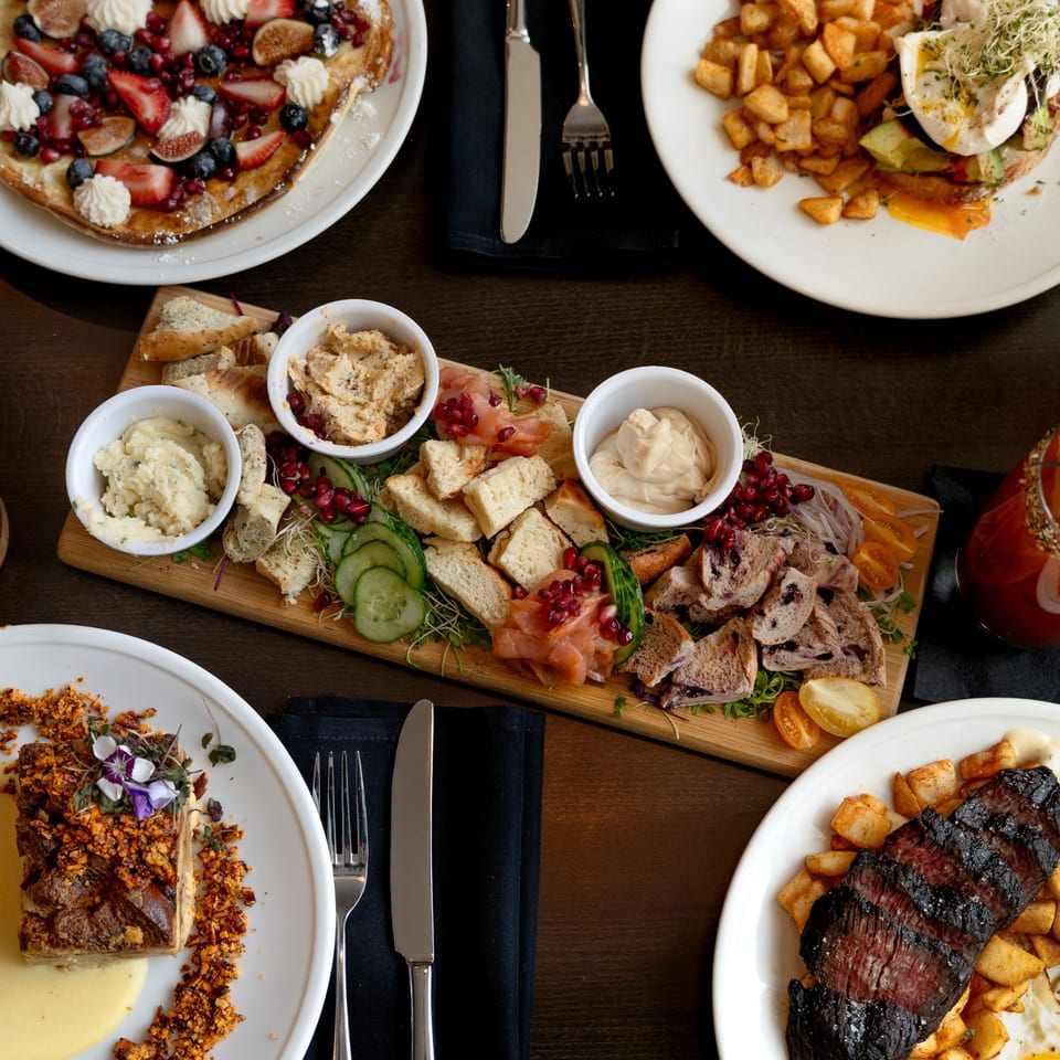 A fine-dining table spread with a charcuterie board, pancakes, steak, and other gourmet dishes.