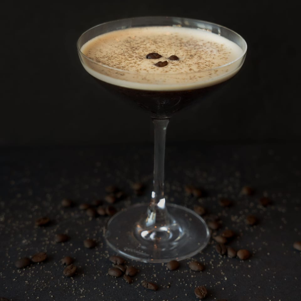 Espresso martini in a coupe glass, garnished with coffee beans and sprinkled sugar on a dark surface.