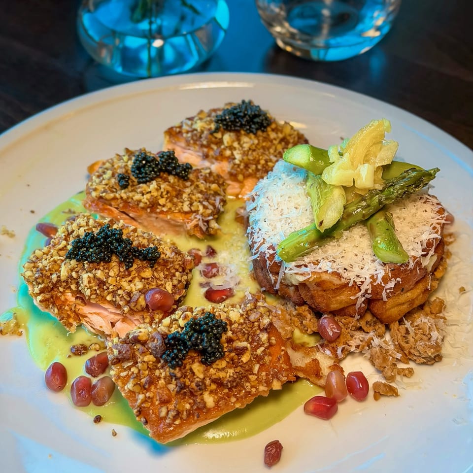 Gourmet dish with salmon, caviar, nuts, asparagus, cheese, and pomegranate seeds on a white plate.
