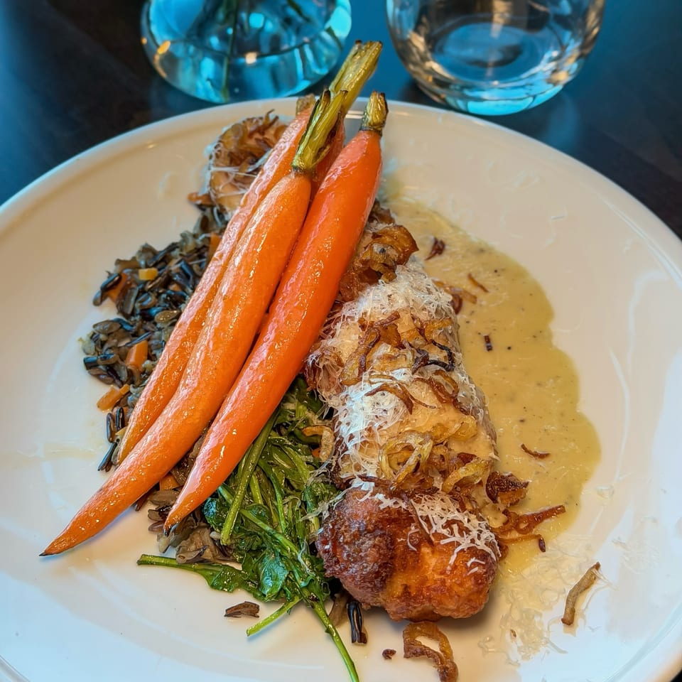 Plated dish with roasted carrots, wild rice, greens, a fried croquette, and creamy sauce.